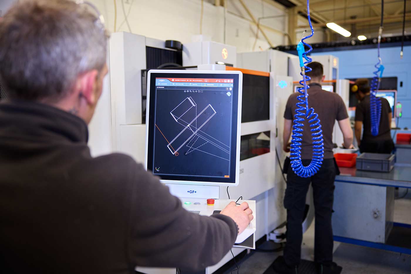 Three male figures seen from behind are all working at different machines in a factory.